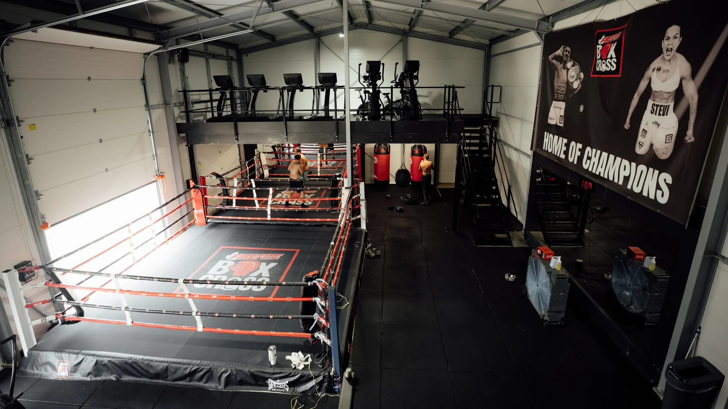 One of the two competition boxing rings at BoxCross UK Wisbech from the mezzanine, heavy bags to one side and the Home of Champions banner behind