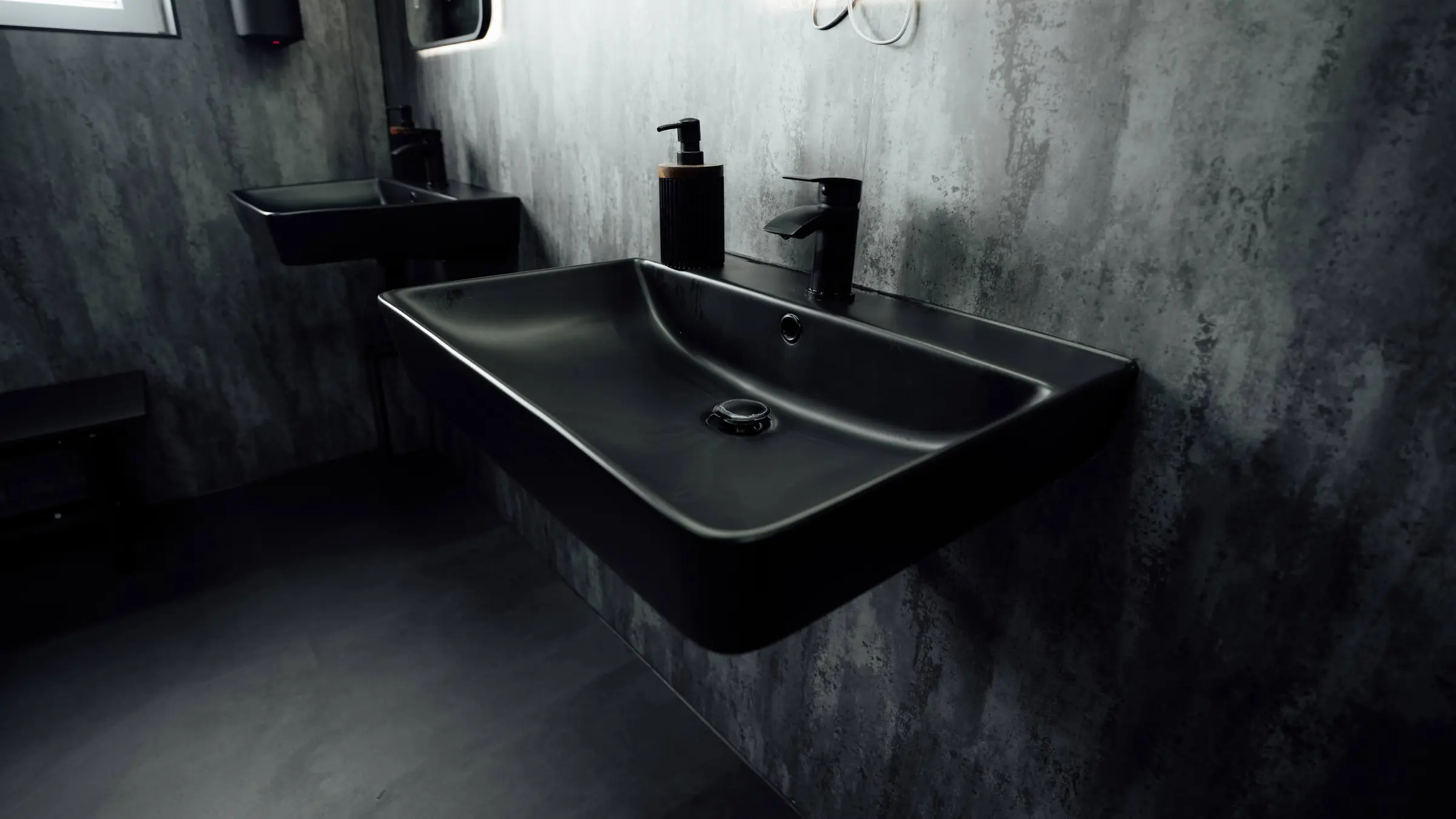 A matte black basin and tap against the concrete-effect wall