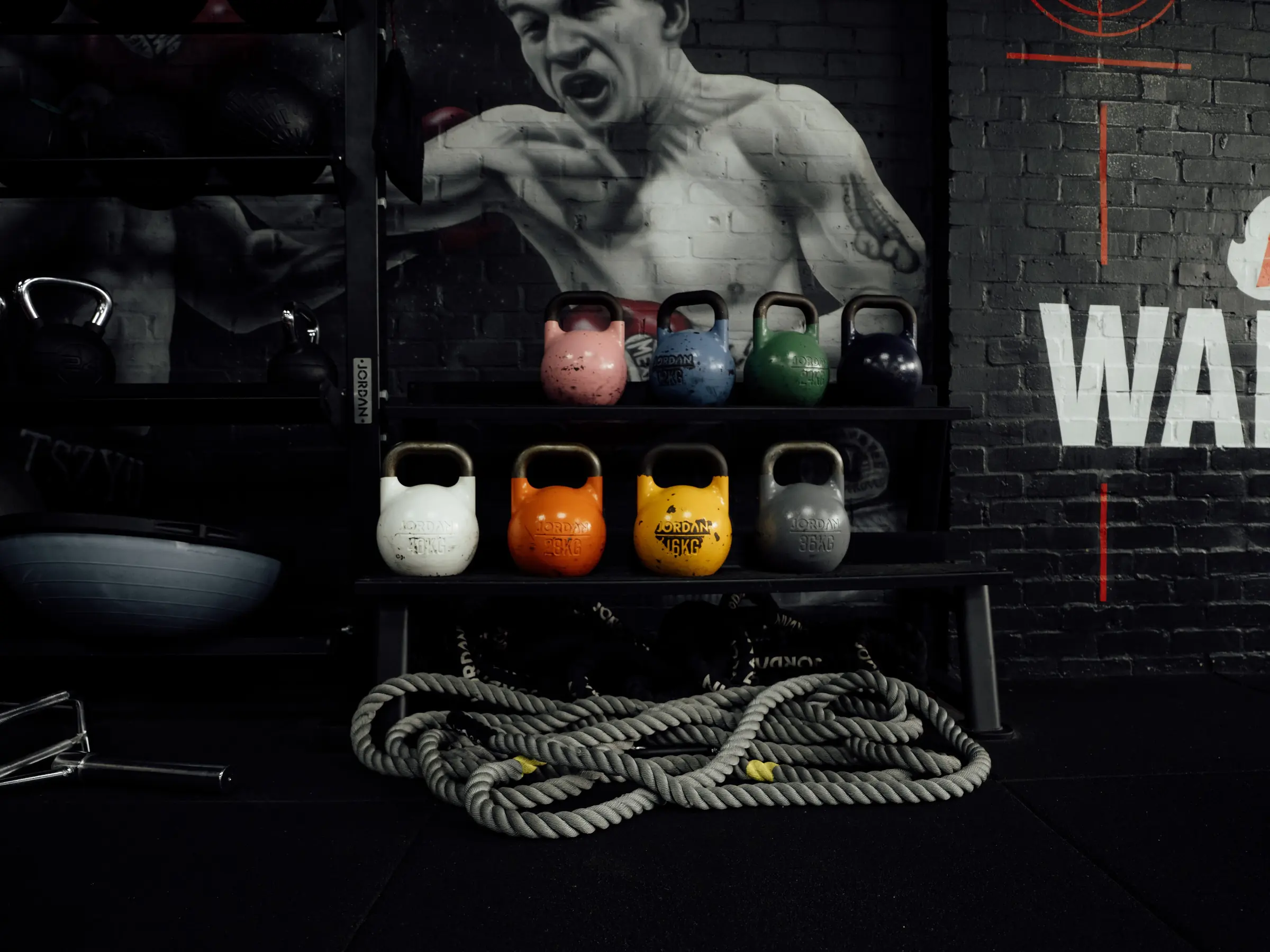 Competition kettlebells and a battle rope beneath the Muhammad Ali mural