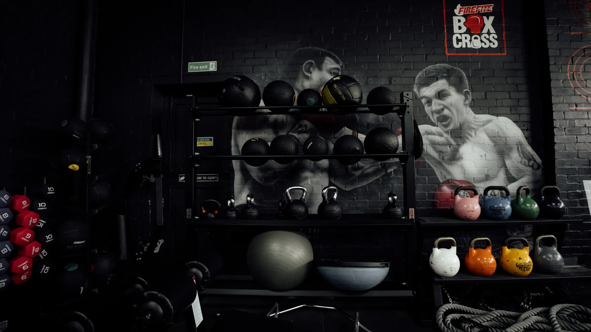 Wall balls racked beneath the Ali mural with kettlebells and a bosu