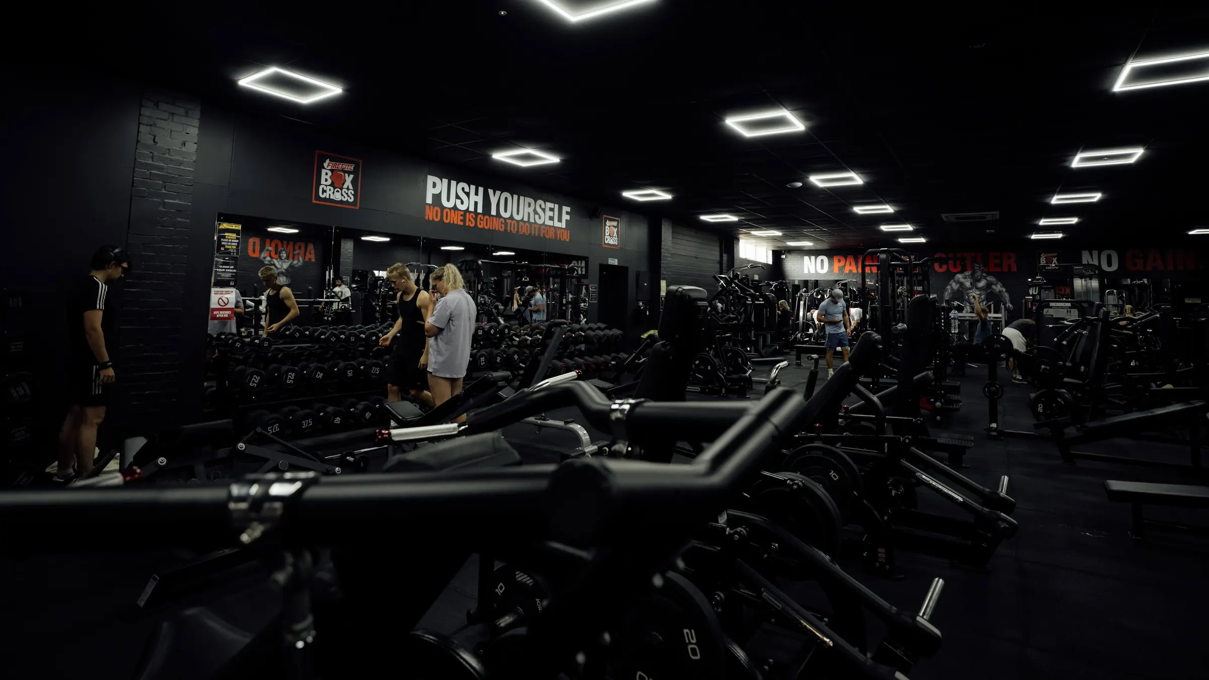 Members at the dumbbells with plate-loaded machines in the foreground on the main floor
