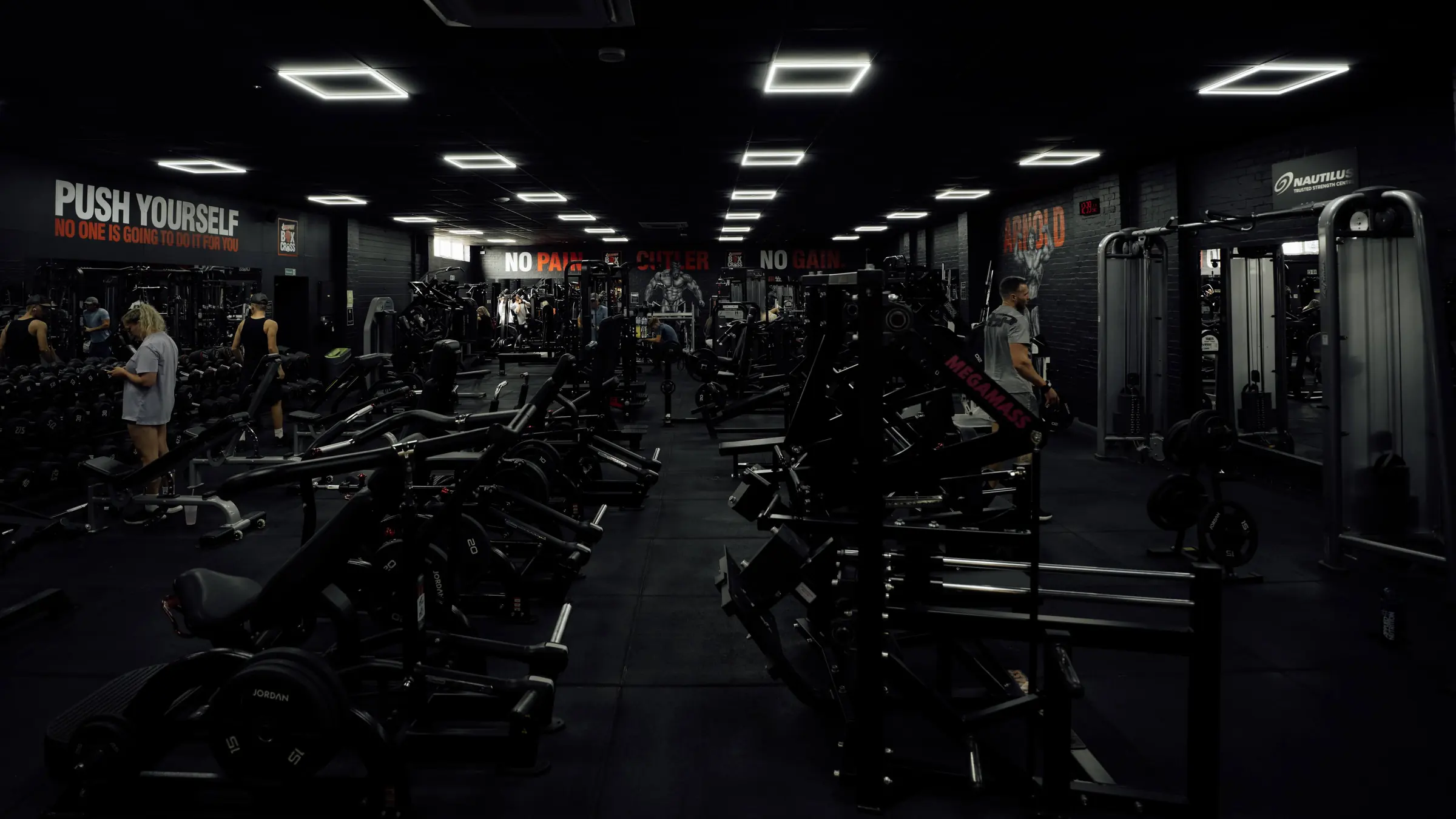 The main training floor at BoxCross UK Wisbech, with rows of plate-loaded machines, dumbbells and cable stations under the Push Yourself and No Pain No Gain murals