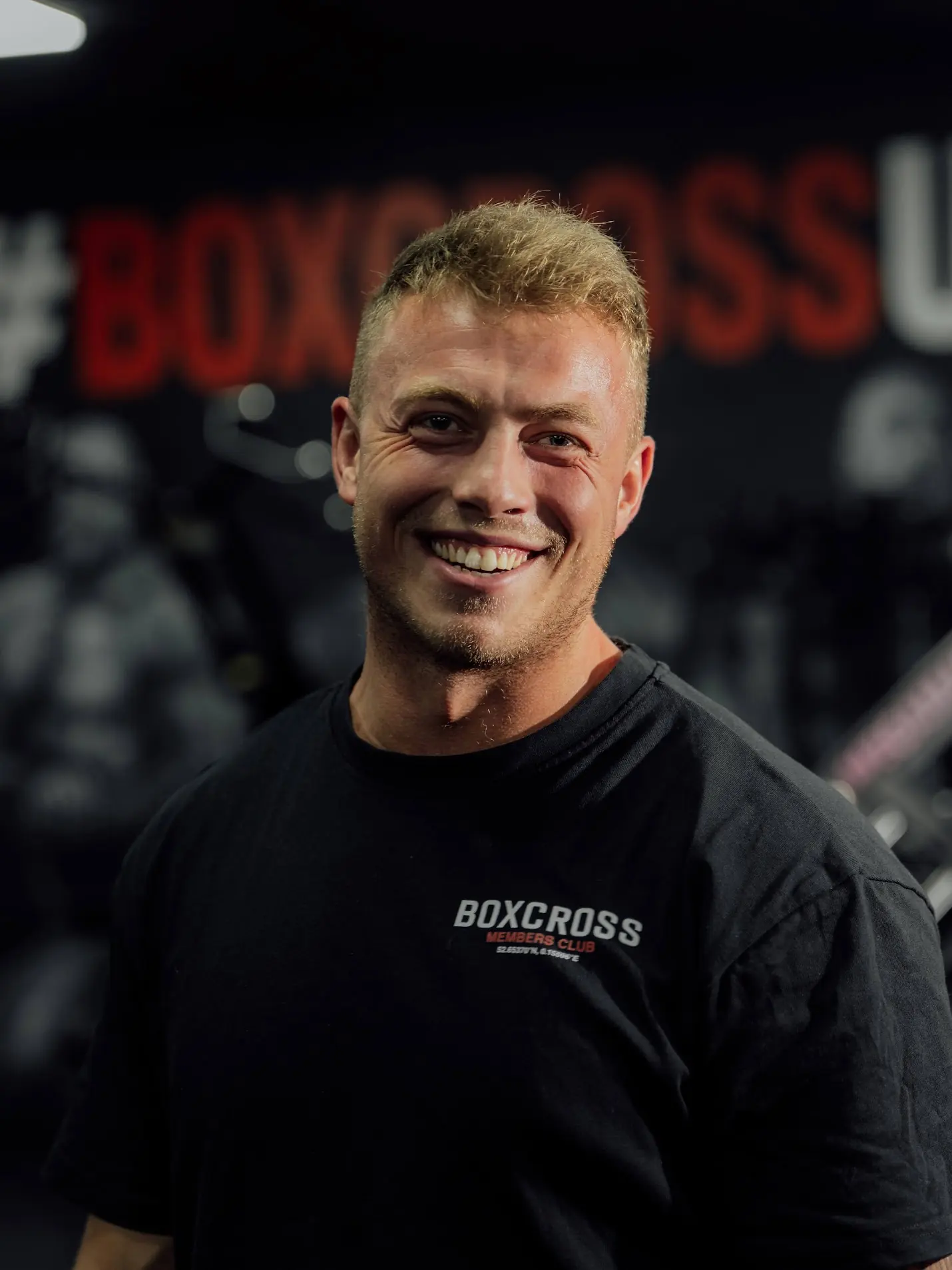 Daniel Higgs, personal trainer at BoxCross UK Wisbech, laughing in front of the #BOXCROSSUK mural