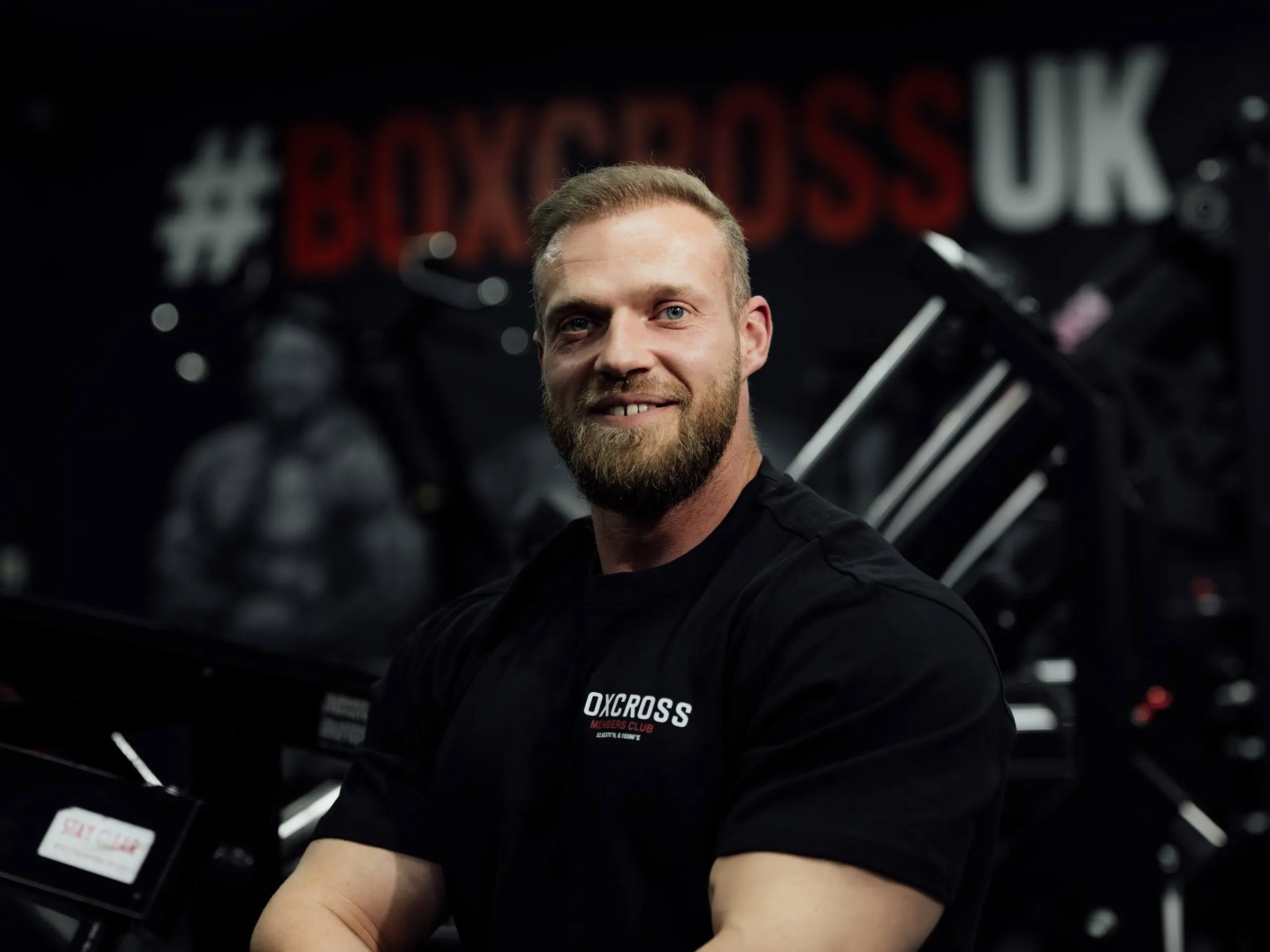 Jack Earle, personal trainer at BoxCross UK Wisbech, seated in front of the #BOXCROSSUK mural