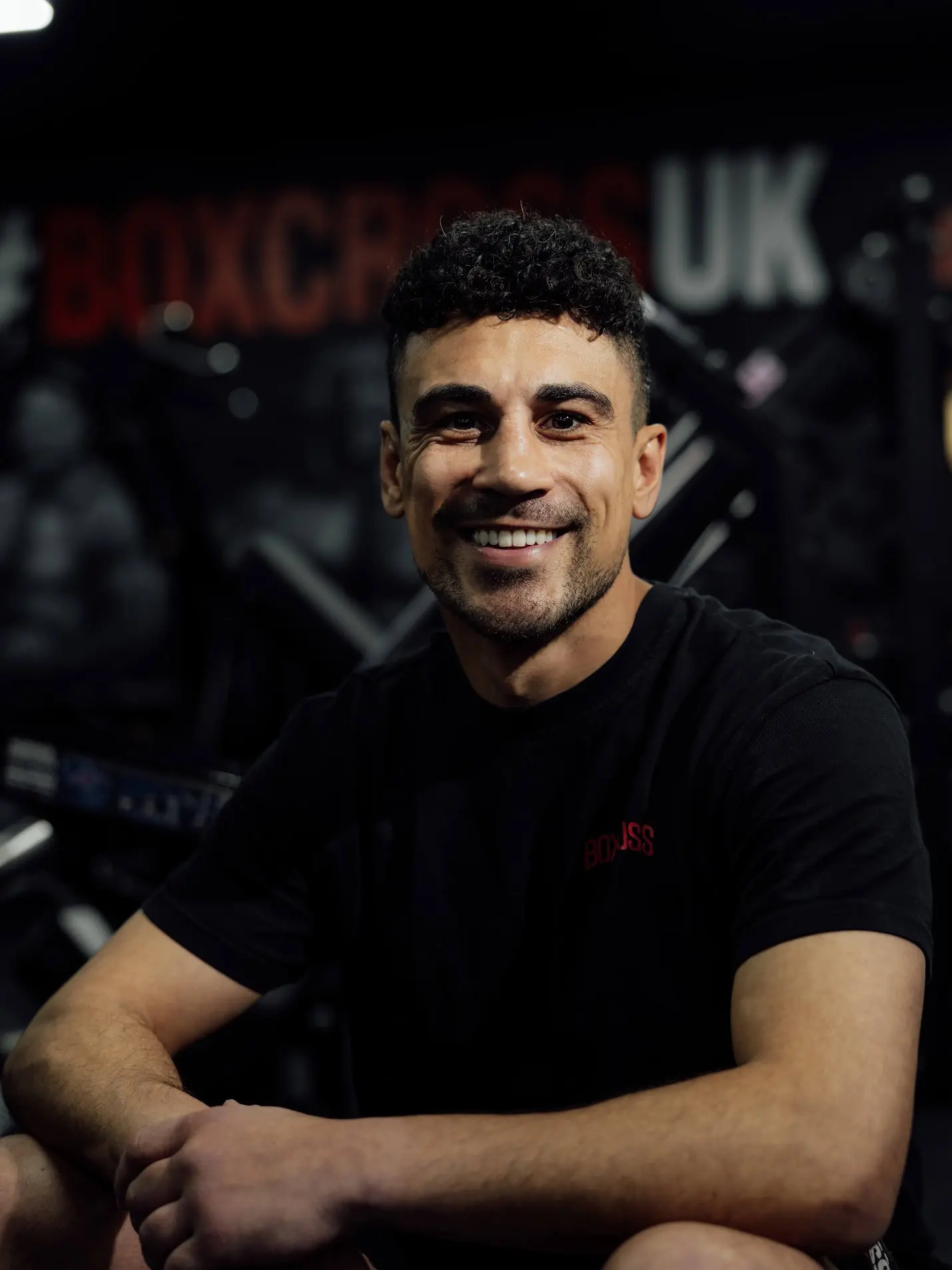 Jordan Gill, professional boxer and co-owner of BoxCross UK, smiling in front of the #BOXCROSSUK mural