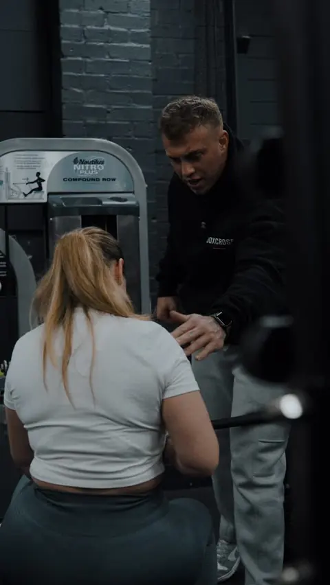 A BoxCross coach correcting a member’s form on the compound row machine